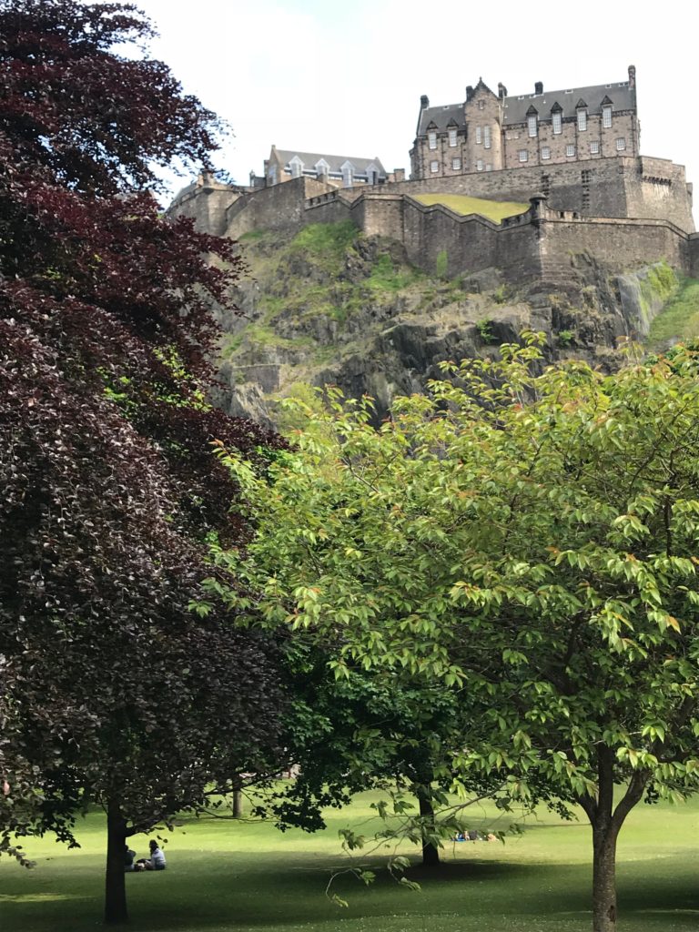 A tree filled park with the Edinburgh Castle perched high above on a rocky cliff in Edinburgh, Scotland