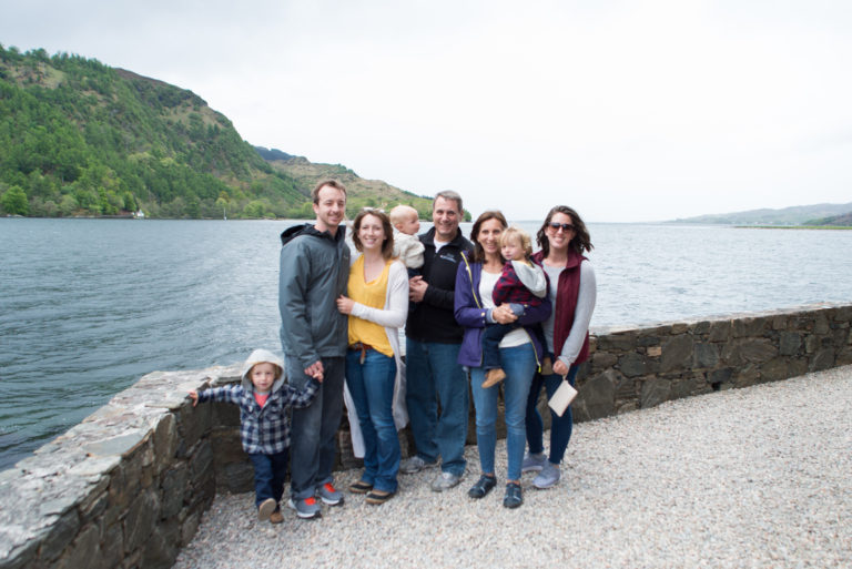 A family standing next to a stone wall next to a loch at the Eilene Donan Castle in Scotland