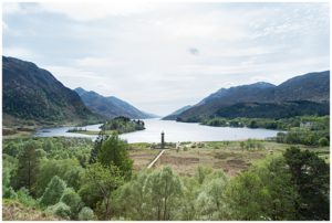 Scottish mountains sloping into a loch with the Glenfinnan Monument on the shoreline in Scotland