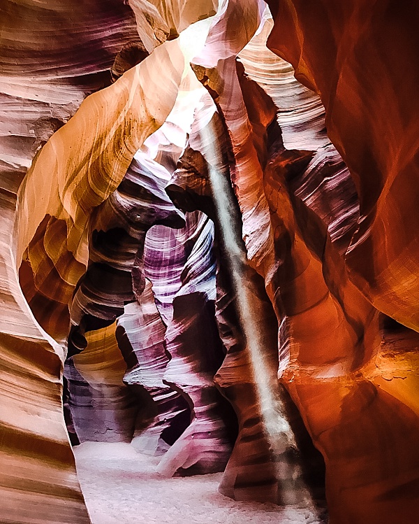 Sunbeams shine through the top of Antelope Canyon and shoot down to the sand path between the stones