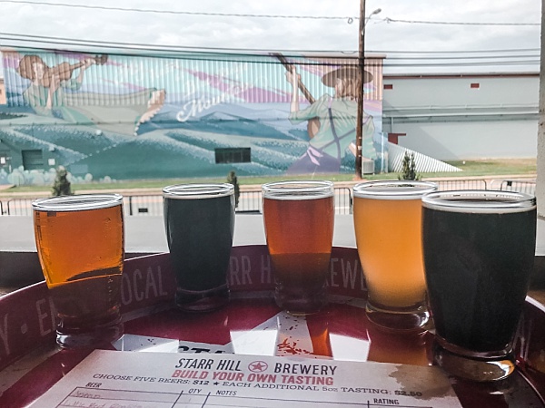 Five Starr Hill Brewery beer samples lined up facing a painted building